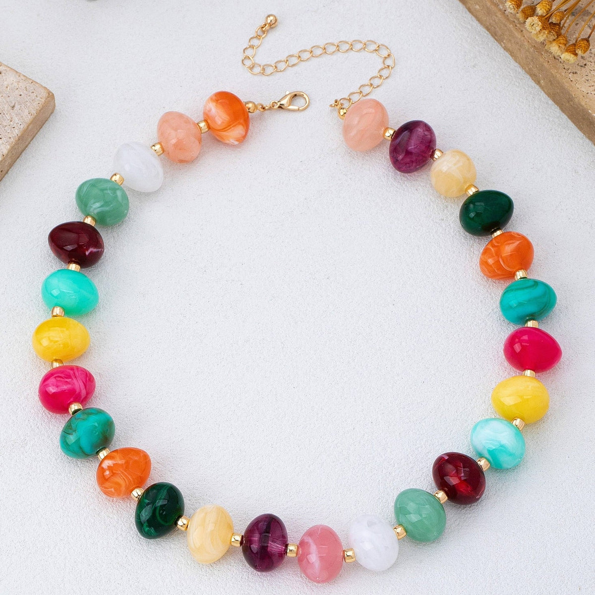 Colorful beaded statement necklace with multicolored pebble-shaped beads and gold-tone spacers, worn with a white top.