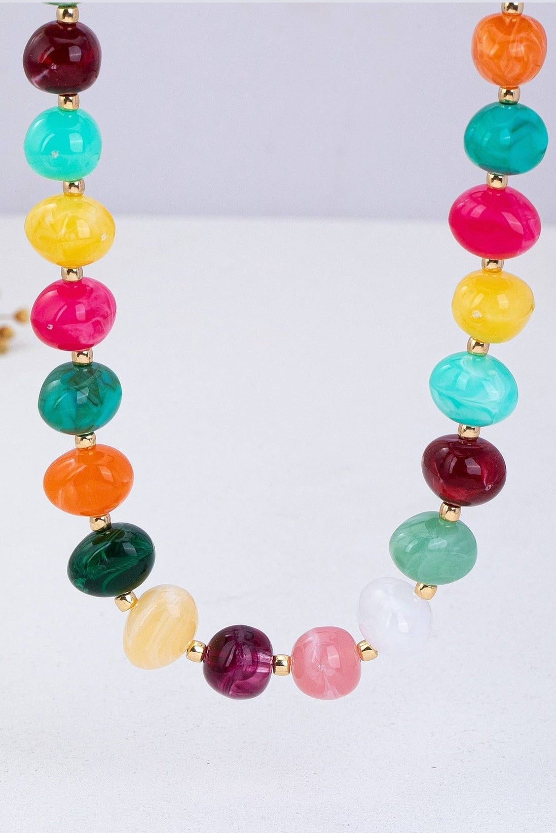 Colorful beaded statement necklace with multicolored pebble-shaped beads and gold-tone spacers, worn with a white top.