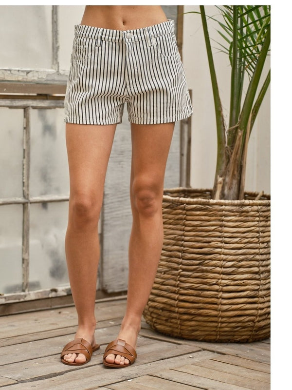 Person wearing black and white striped shorts standing on a wooden deck with a plant in the background.