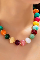 Colorful beaded statement necklace with multicolored pebble-shaped beads and gold-tone spacers, worn with a white top.