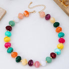 Colorful beaded statement necklace with multicolored pebble-shaped beads and gold-tone spacers, worn with a white top.
