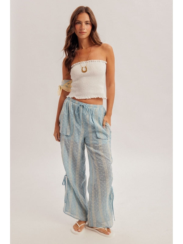 Woman wearing a white strapless top and light blue checkered pants on a plain background