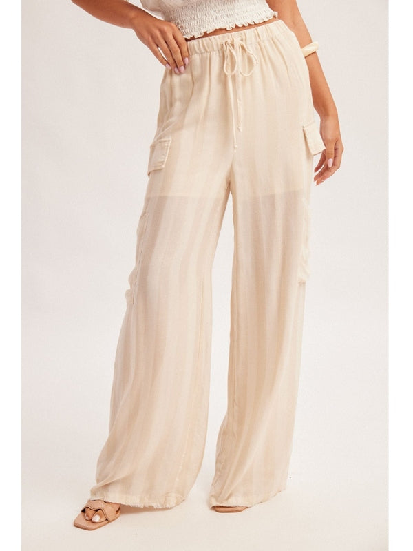 Woman wearing a white strapless top and beige wide-leg pants with a straw hat on a light gray background
