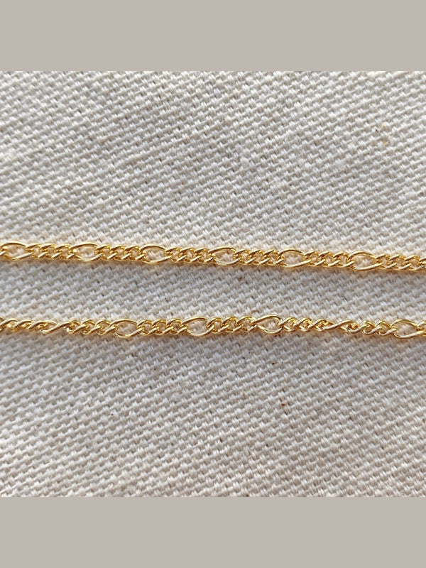 Two gold chains on a textured beige fabric background