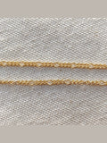 Two gold chains on a textured beige fabric background