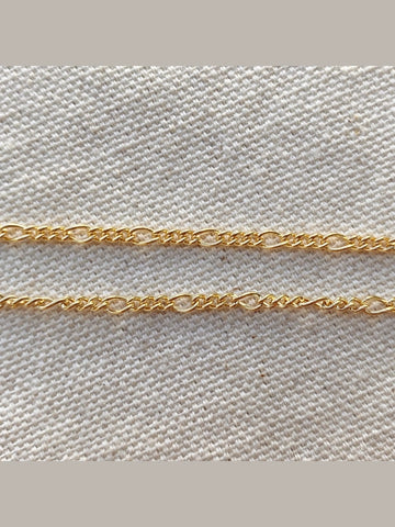Two gold chains on a textured beige fabric background