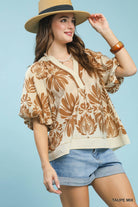 Woman wearing a beige floral blouse, denim shorts, and a straw hat on a light blue background.