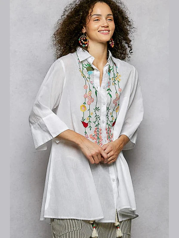 Woman wearing a white shirt with floral embroidery on a gray background