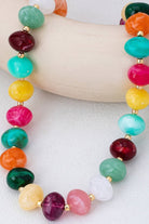 Colorful beaded statement necklace with multicolored pebble-shaped beads and gold-tone spacers, worn with a white top.