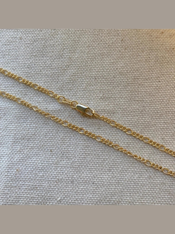 Two gold chains on a textured beige fabric background