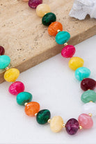 Colorful beaded statement necklace with multicolored pebble-shaped beads and gold-tone spacers, worn with a white top.