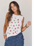 Woman wearing a sleeveless top with strawberry pattern and blue jeans against a plain background