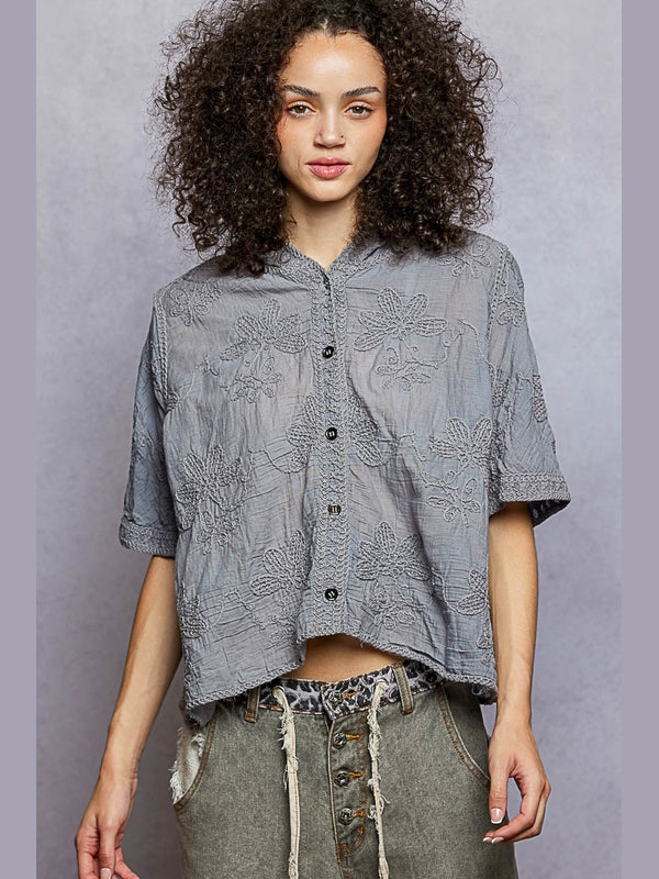 Woman wearing a gray patterned shirt with rolled-up sleeves against a gray background