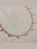 Delicate gold necklace with small pendants on a textured beige background