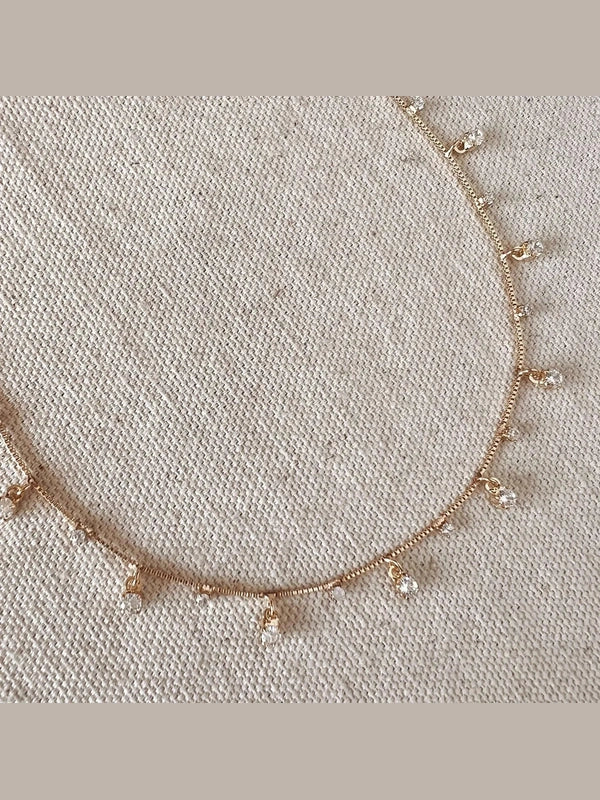 Delicate gold necklace with small pendants on a textured beige background