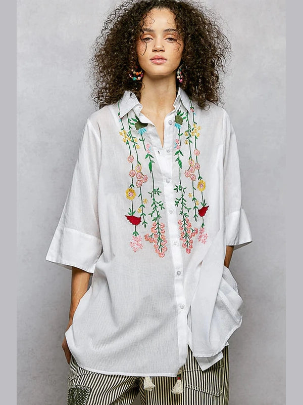Woman wearing a white shirt with floral embroidery on a gray background