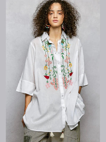 Woman wearing a white shirt with floral embroidery on a gray background
