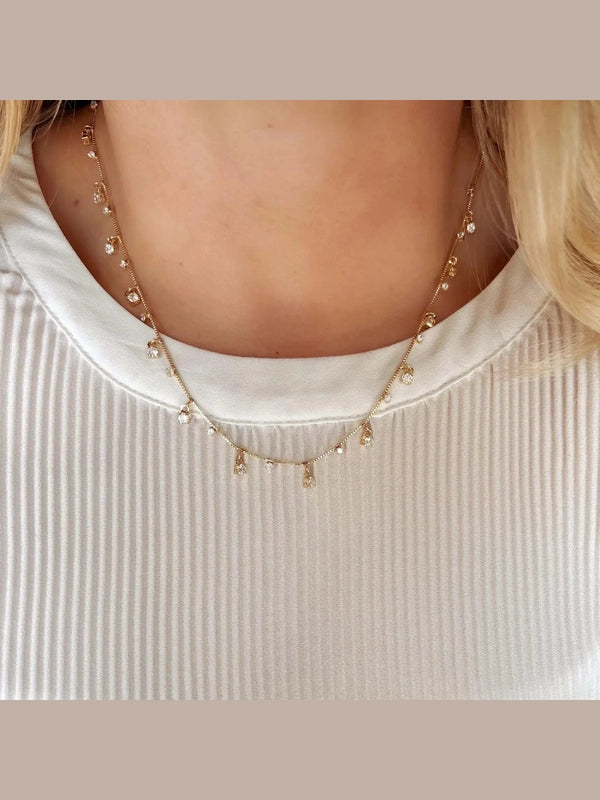 Delicate gold necklace with small pendants on a textured beige background