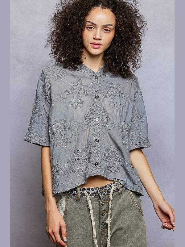 Woman wearing a gray patterned shirt with rolled-up sleeves against a gray background