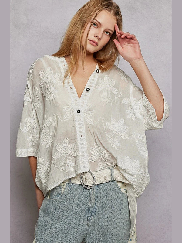 Woman wearing a light-colored floral blouse and light blue pants against a gray background