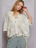 Woman wearing a light-colored floral blouse and light blue pants against a gray background